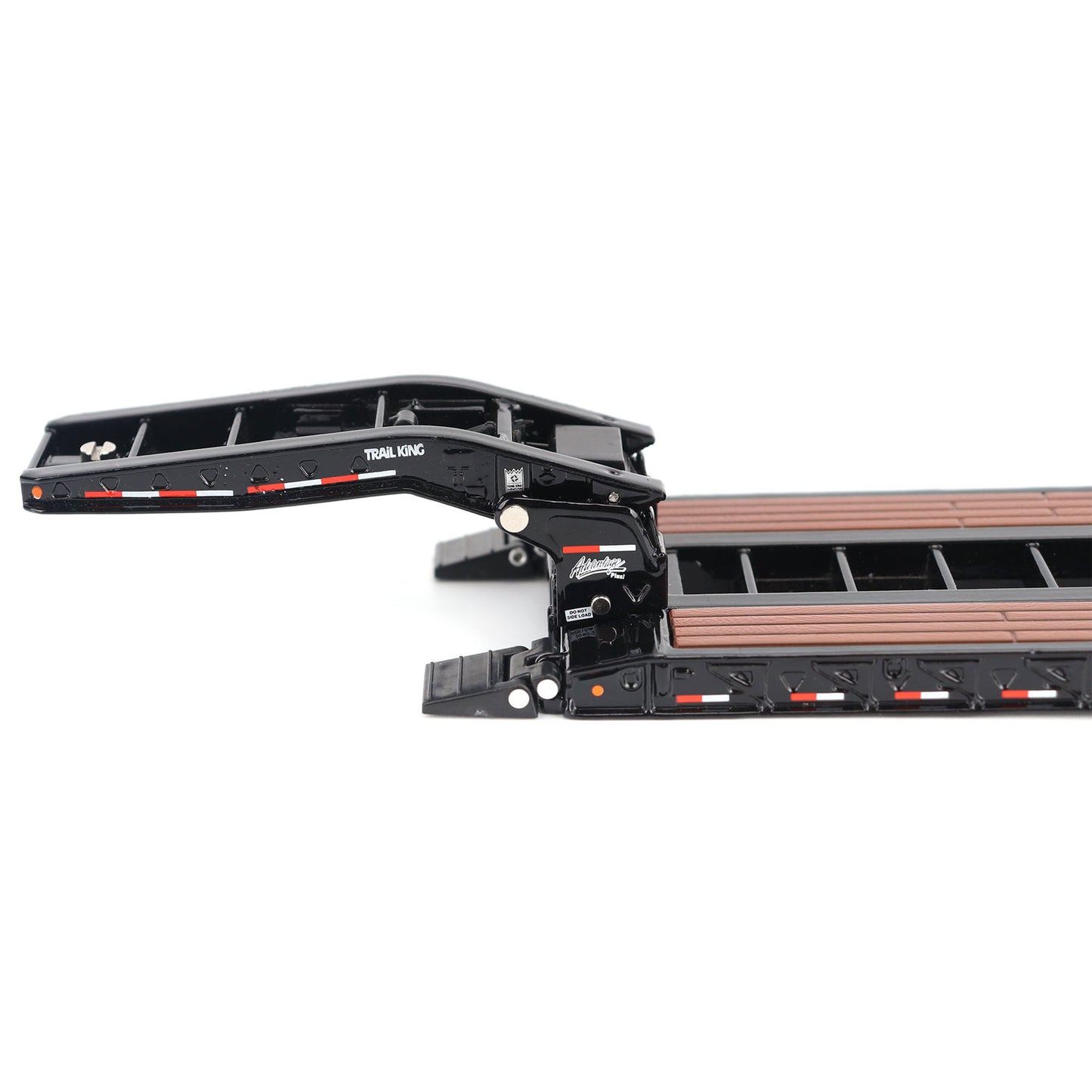 A miniature toy model of a Trail King TK120 lowboy trailer with a black frame, brown textured deck, and a yellow sign, shown on a solid white background.