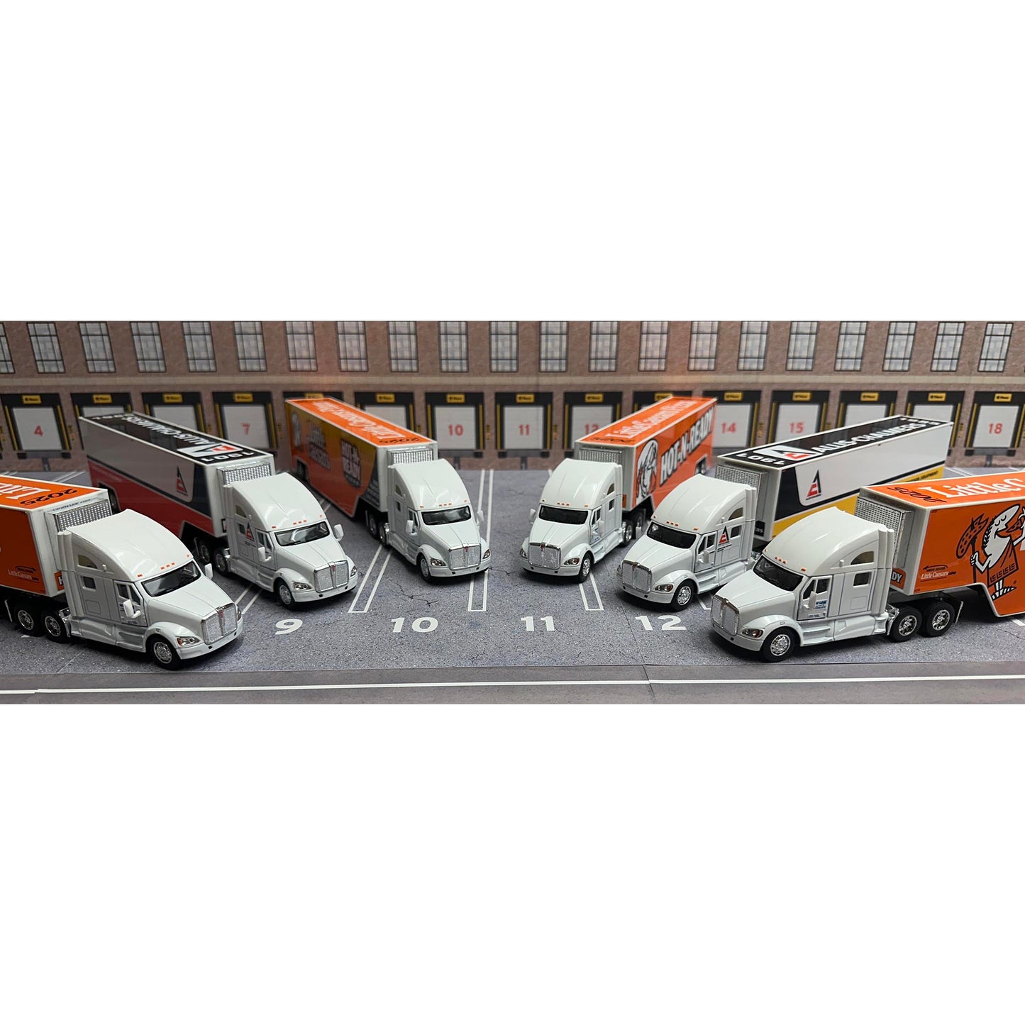 Model trucks arranged in a parking lot with a building in the background