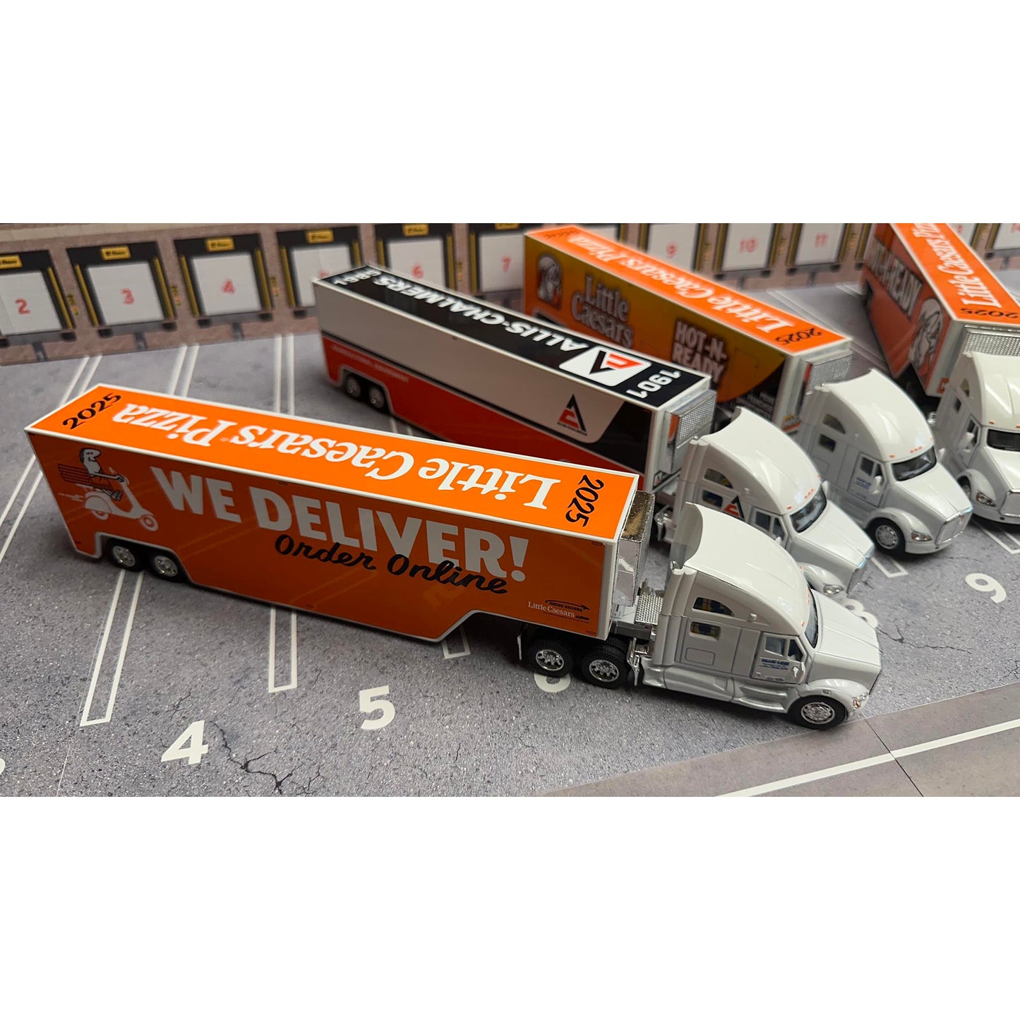 Model trucks with Little Caesars Pizza and Allis Chalmers branding on a parking lot background.