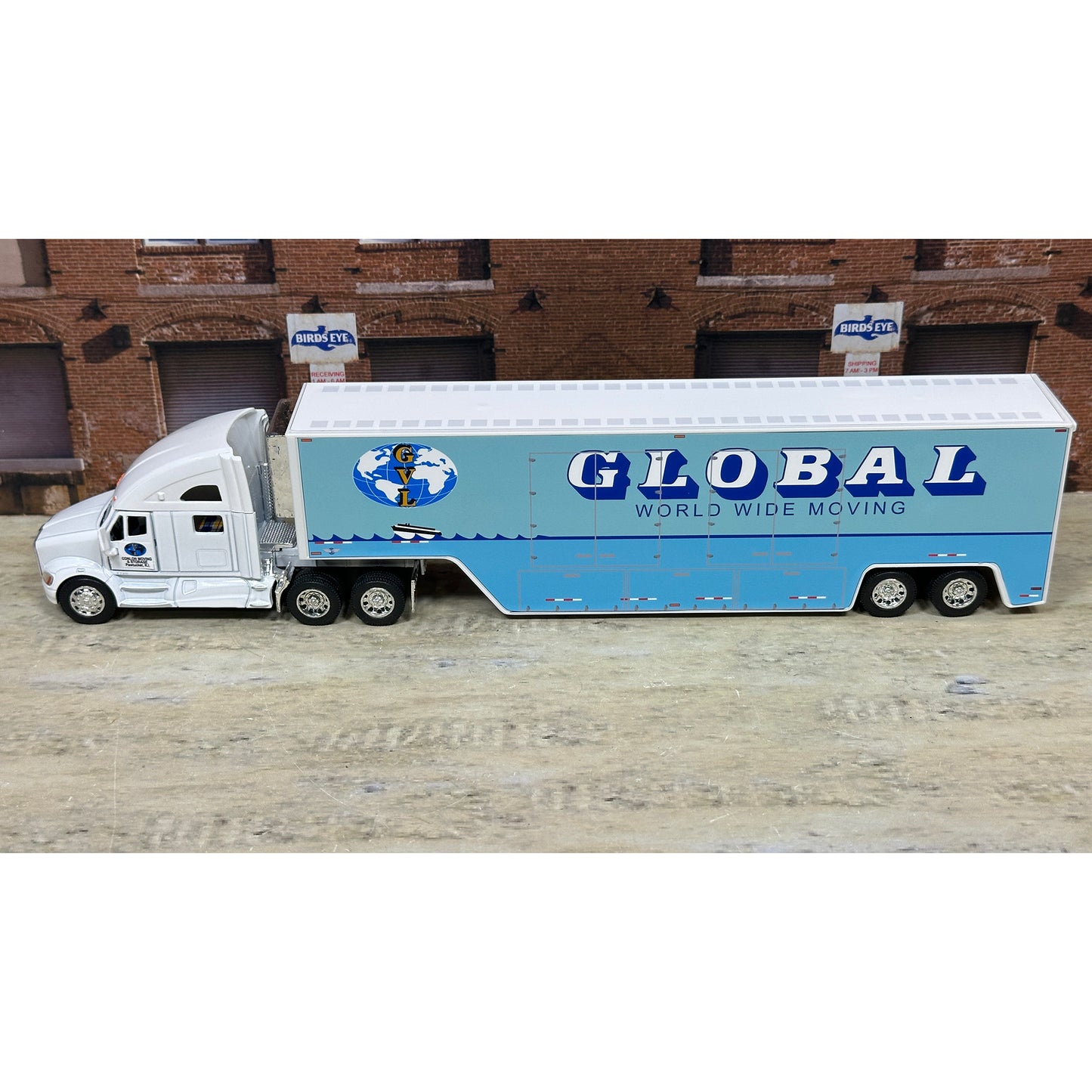 Model truck with 'Global World Wide Moving' on a wooden surface with a brick building in the background.