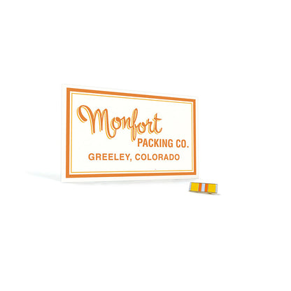 Collector card with Monfort Packing Co. Greeley, Colorado printed in Orange lettering and a yellow, orange, and white shirt pin photographed on a white background