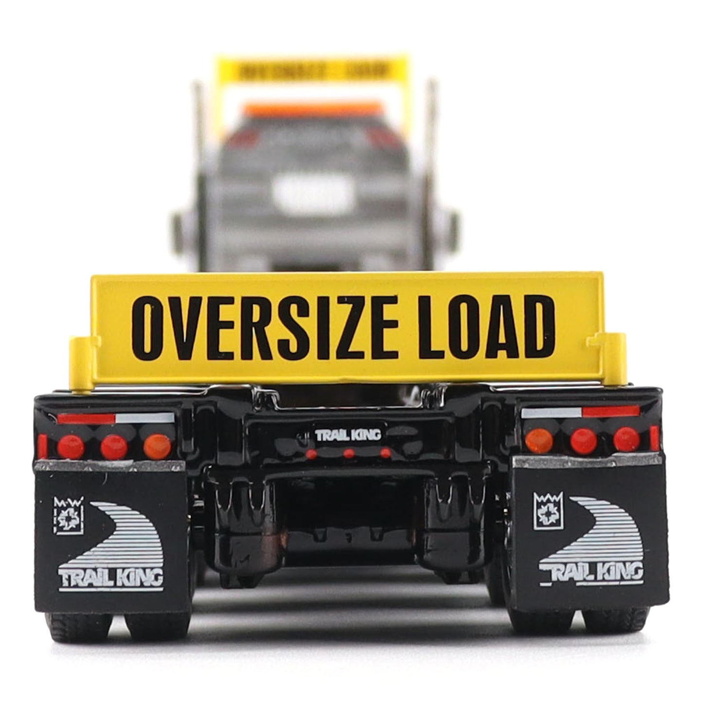 A miniature toy model of a Trail King semi-truck rear, featuring a black chassis with black mudflaps, red taillights, and a prominent yellow sign reading 'OVERSIZE LOAD' in black text.