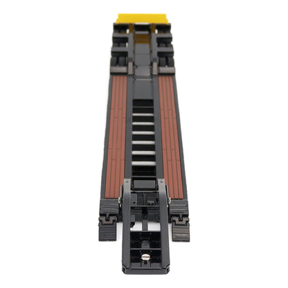 A miniature toy model of a Trail King TK120 lowboy trailer with a black frame, brown textured deck, and a yellow sign, shown on a solid white background.