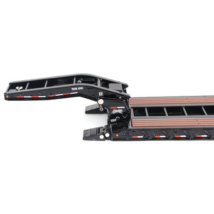 A miniature toy model of a Trail King TK120 lowboy trailer with a black frame, brown textured deck, and a yellow sign, shown on a solid white background.