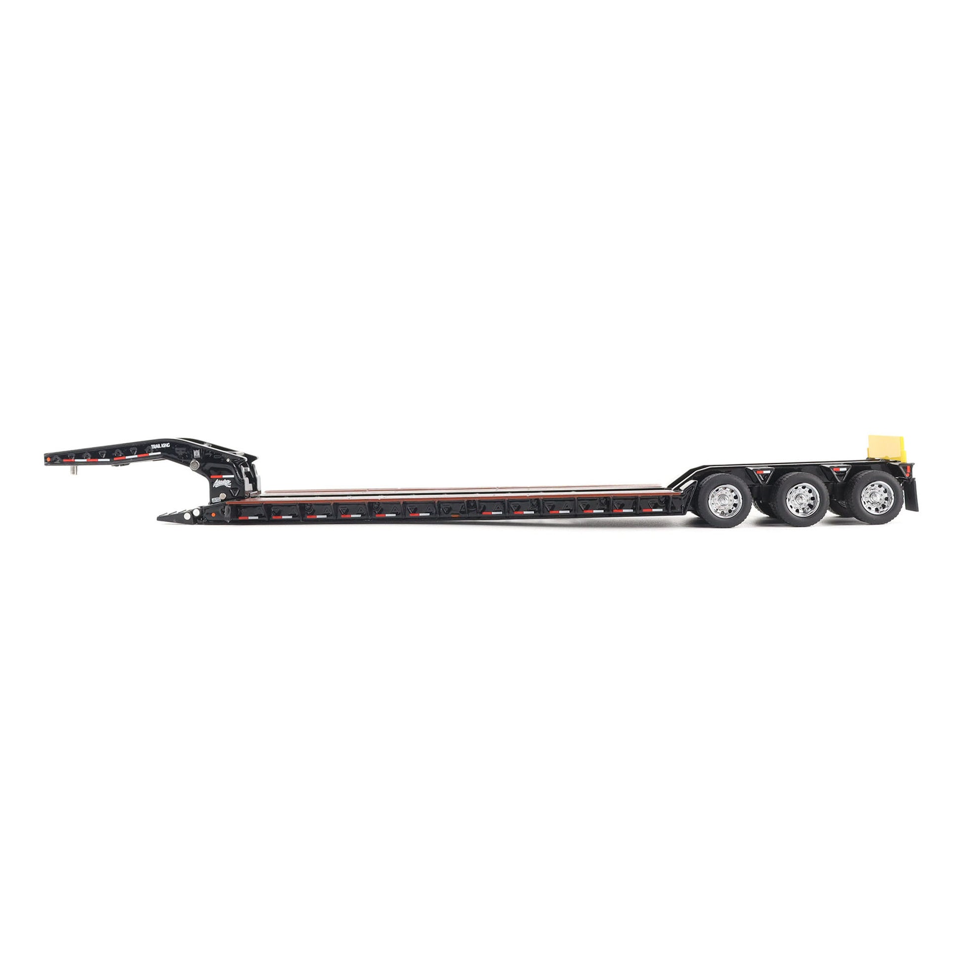 A miniature toy model of a Trail King TK120 lowboy trailer with a black frame, brown textured deck, and a yellow sign, shown on a solid white background.