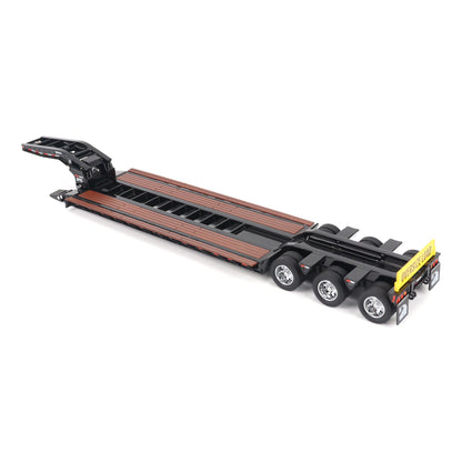 A miniature toy model of a Trail King TK120 lowboy trailer with a black frame, brown textured deck, and a yellow sign, shown on a solid white background.