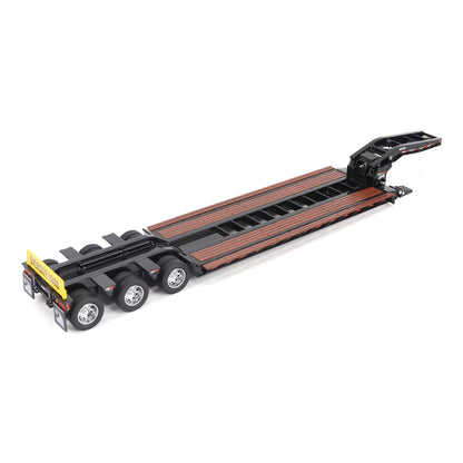 A miniature toy model of a Trail King TK120 lowboy trailer with a black frame, brown textured deck, and a yellow sign, shown on a solid white background.