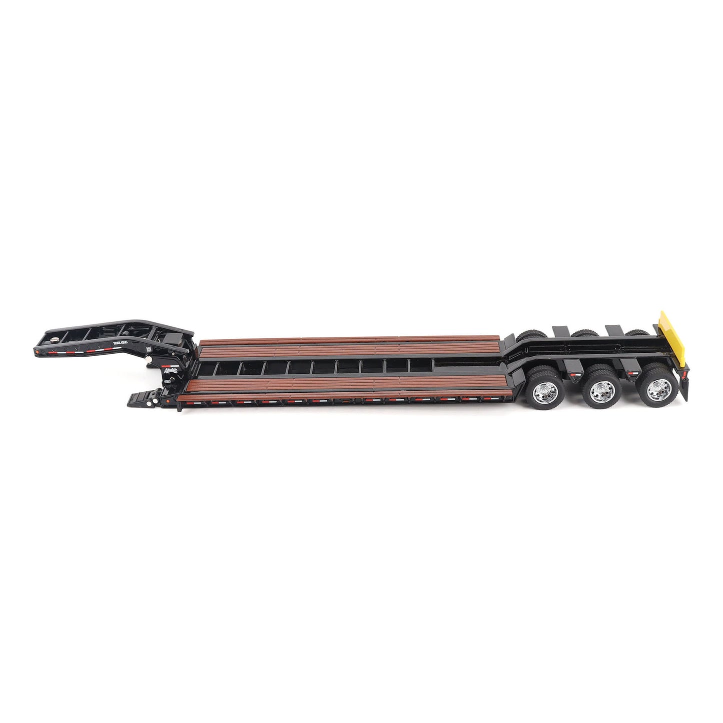 A miniature toy model of a Trail King TK120 lowboy trailer with a black frame, brown textured deck, and a yellow sign, shown on a solid white background.