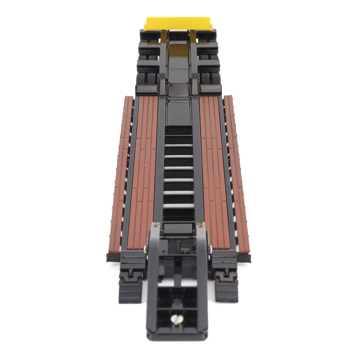 A miniature toy model of a Trail King TK120 lowboy trailer with a black frame, brown textured deck, and a yellow sign, shown on a solid white background.