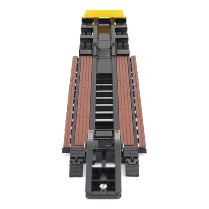 A miniature toy model of a Trail King TK120 lowboy trailer with a black frame, brown textured deck, and a yellow sign, shown on a solid white background.