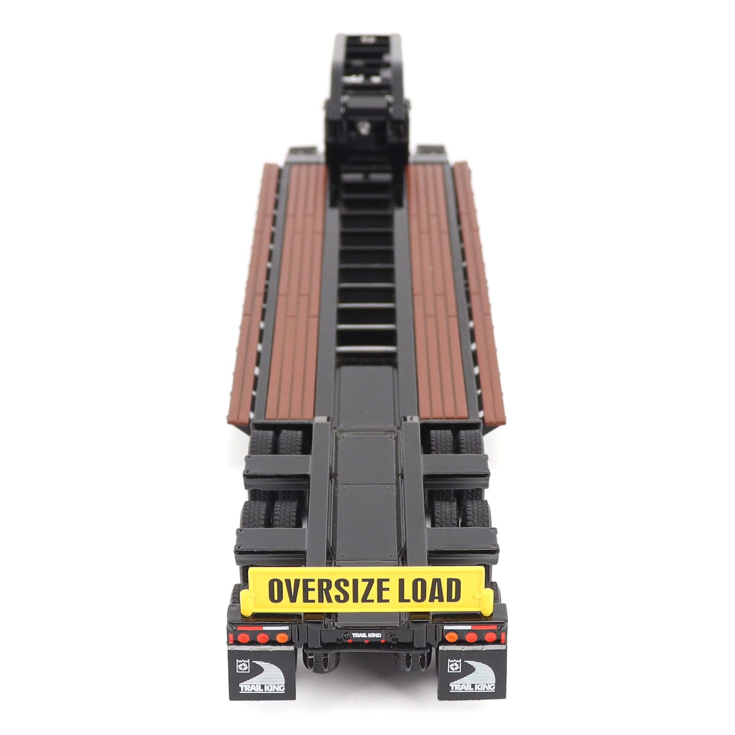 A miniature toy model of a Trail King TK120 lowboy trailer with a black frame, brown textured deck, and a yellow sign, shown on a solid white background.