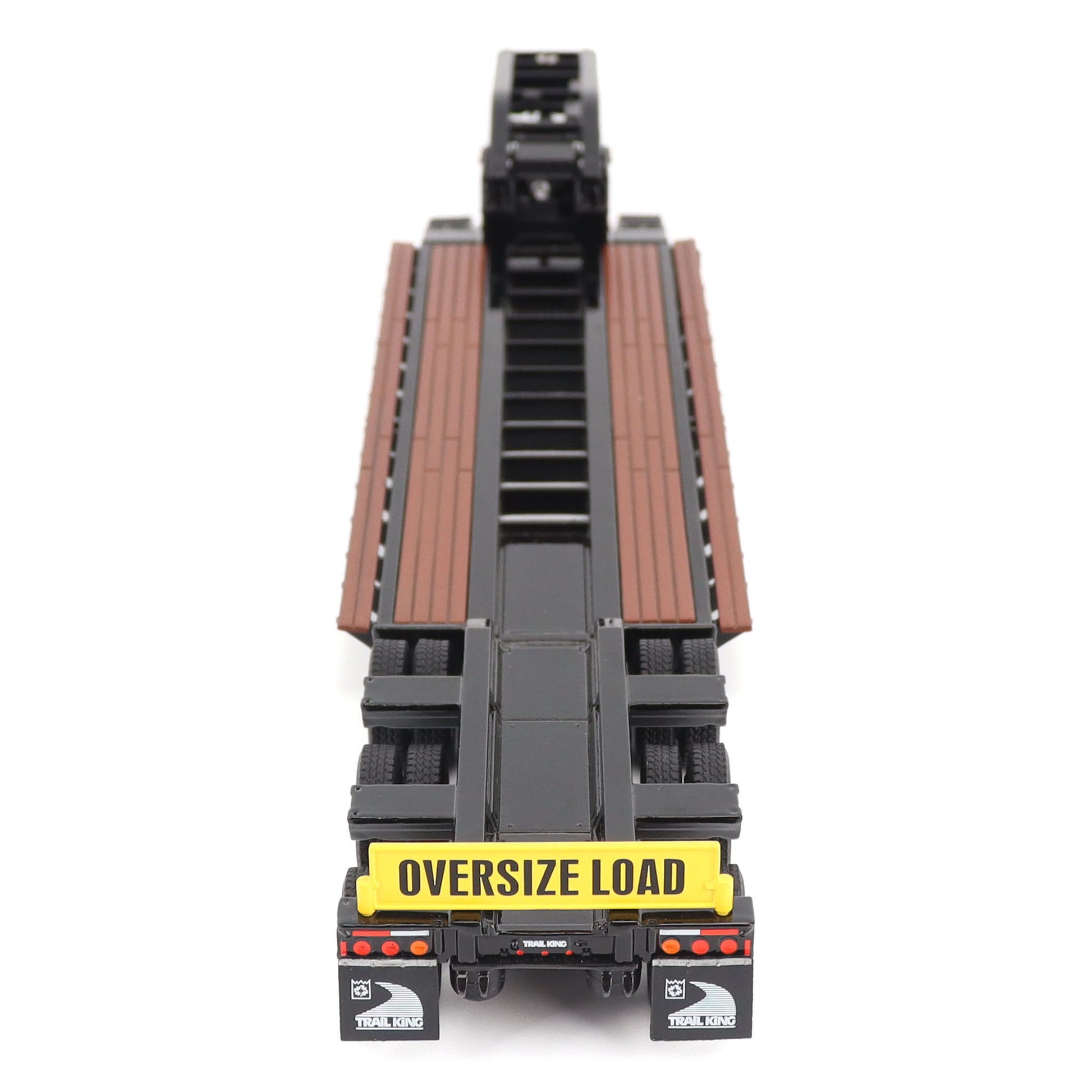 A miniature toy model of a Trail King TK120 lowboy trailer with a black frame, brown textured deck, and a yellow sign, shown on a solid white background.