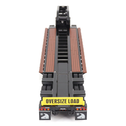 A miniature toy model of a Trail King TK120 lowboy trailer with a black frame, brown textured deck, and a yellow sign, shown on a solid white background.