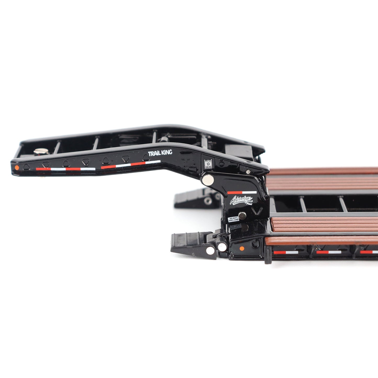 A miniature toy model of a Trail King TK120 lowboy trailer with a black frame, brown textured deck, and a yellow sign, shown on a solid white background.