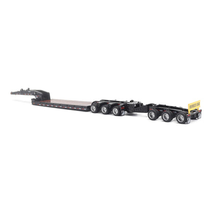 A miniature toy model of a Trail King TK120 lowboy trailer with a black frame, brown textured deck, and a yellow sign, shown on a solid white background.