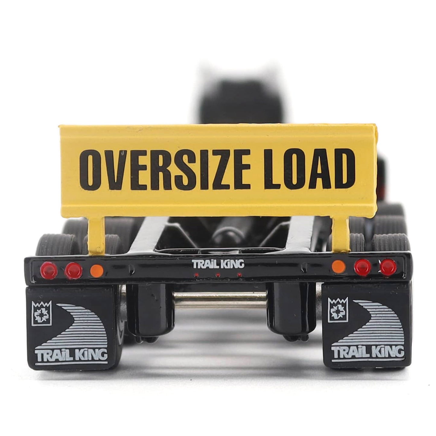 A miniature toy model of a Trail King TK120 lowboy trailer with a black frame, brown textured deck, and a yellow sign, shown on a solid white background.