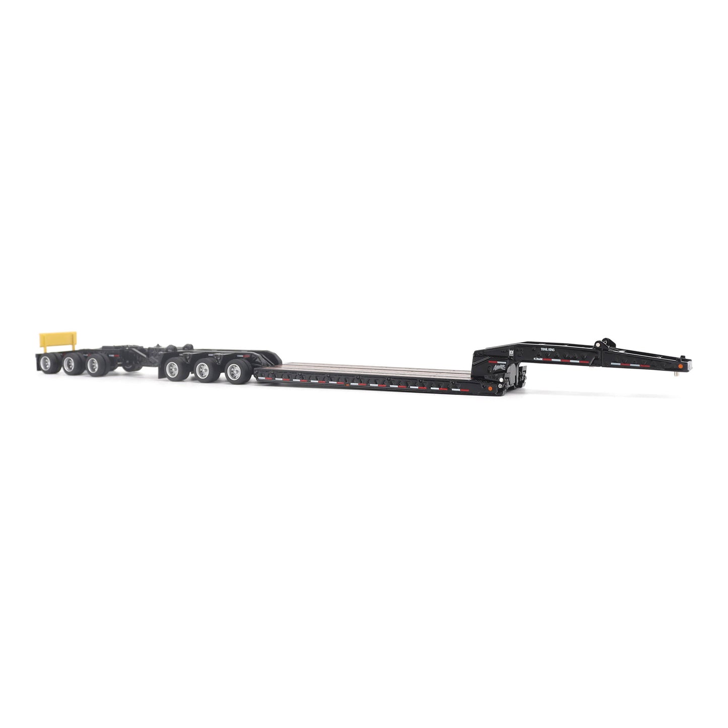 A miniature toy model of a Trail King TK120 lowboy trailer with a black frame, brown textured deck, and a yellow sign, shown on a solid white background.