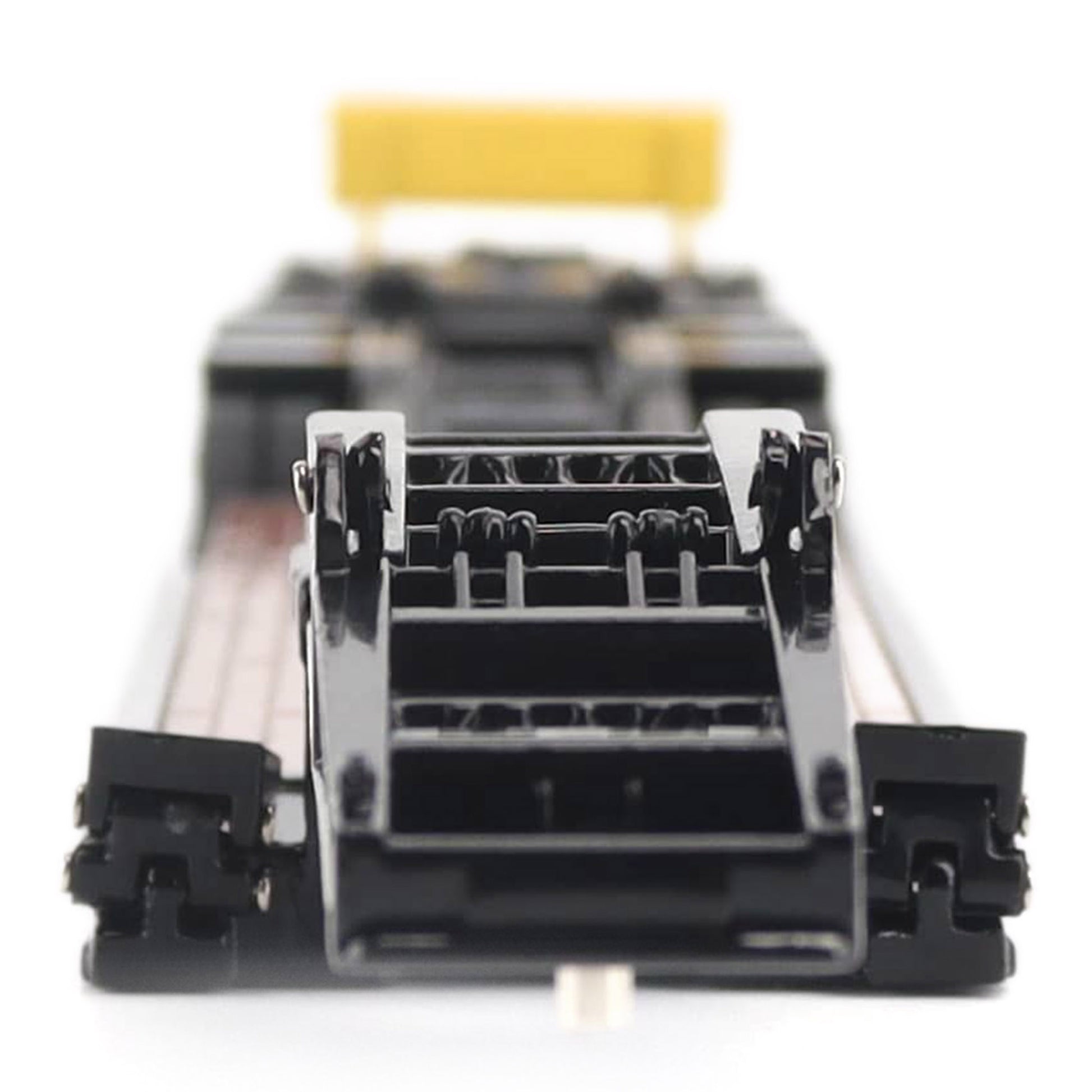 A miniature toy model of a Trail King TK120 lowboy trailer with a black frame, brown textured deck, and a yellow sign, shown on a solid white background.