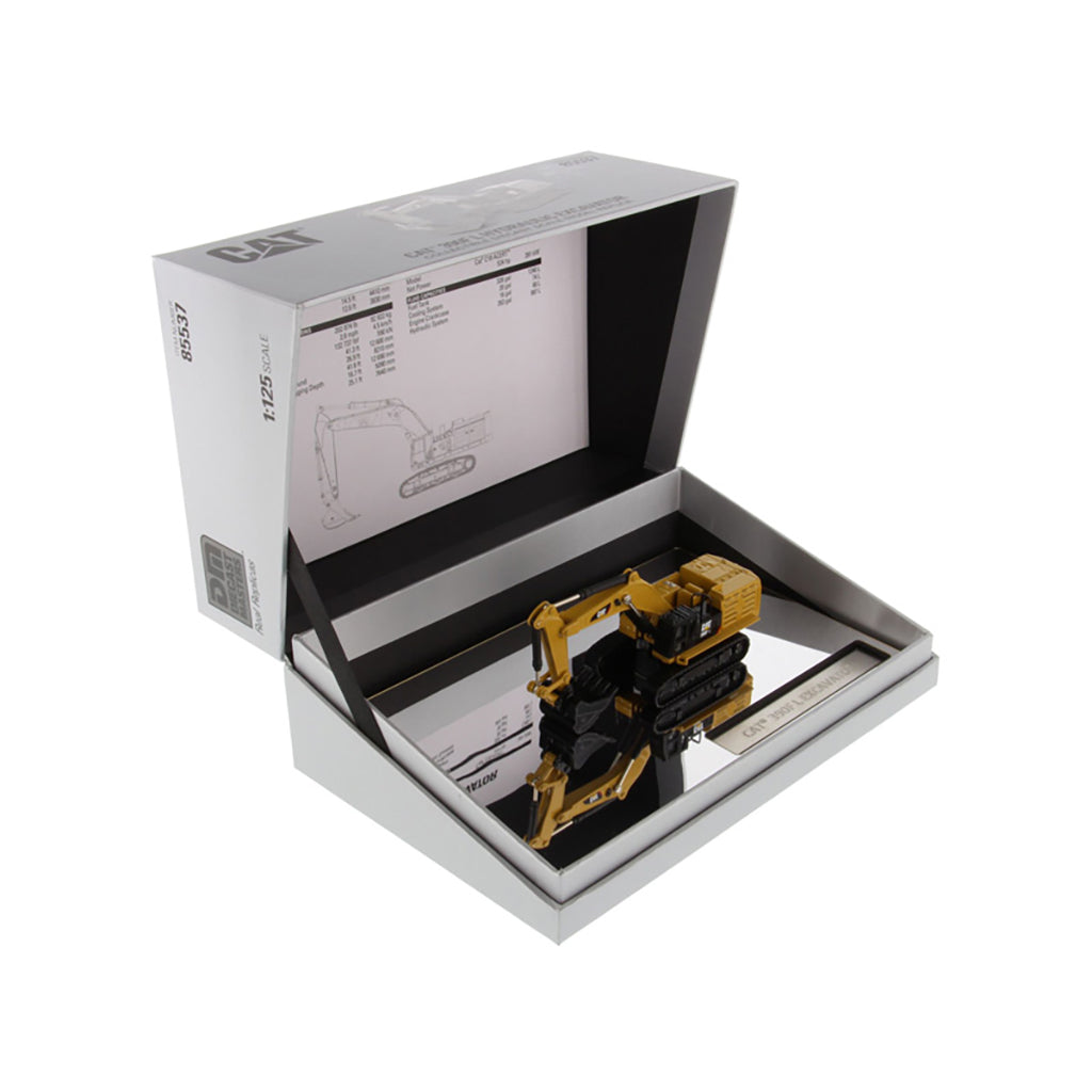 A yellow and black excavator model displayed inside an open silver presentation box with printed inserts and a mirror base, photographed on a white background.
