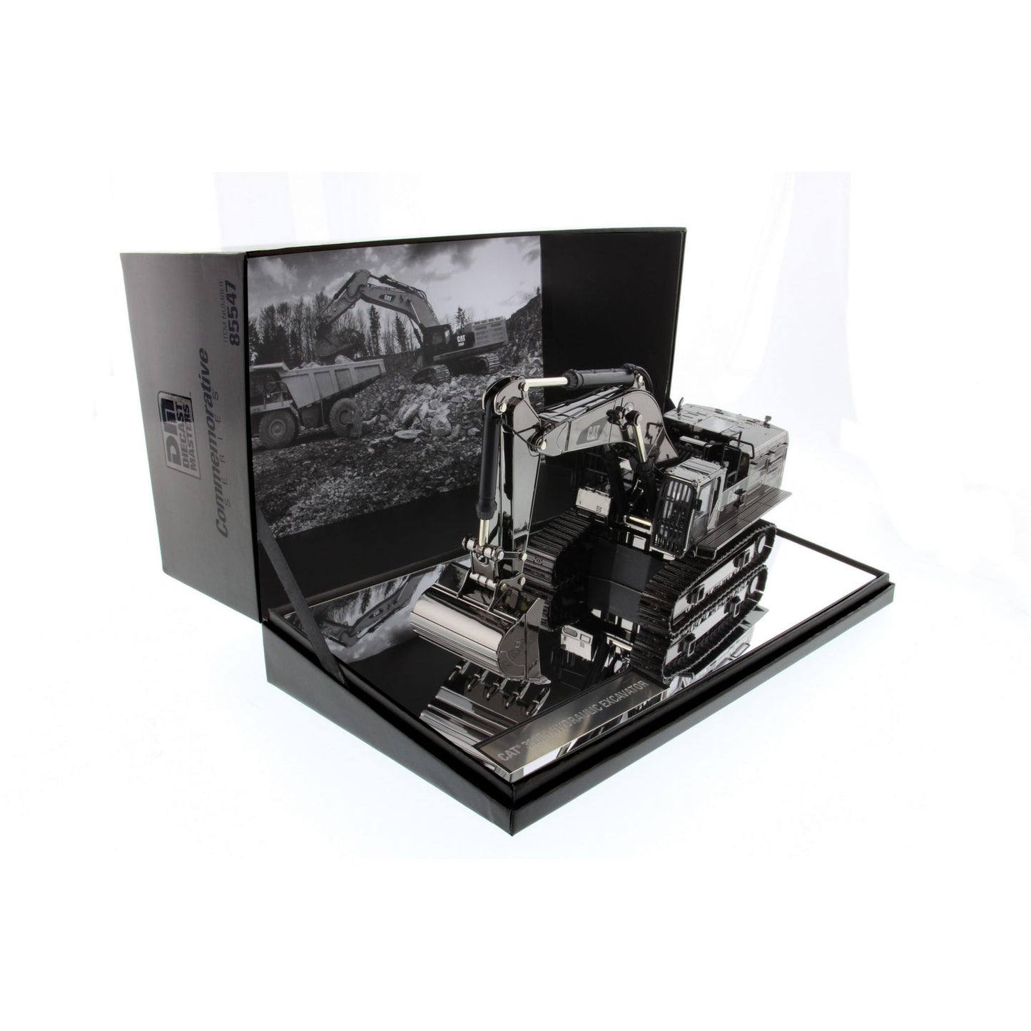 A  model of a black and silver excavator displayed inside its open black presentation box, which features a black-and-white construction scene printed on the inner flap.