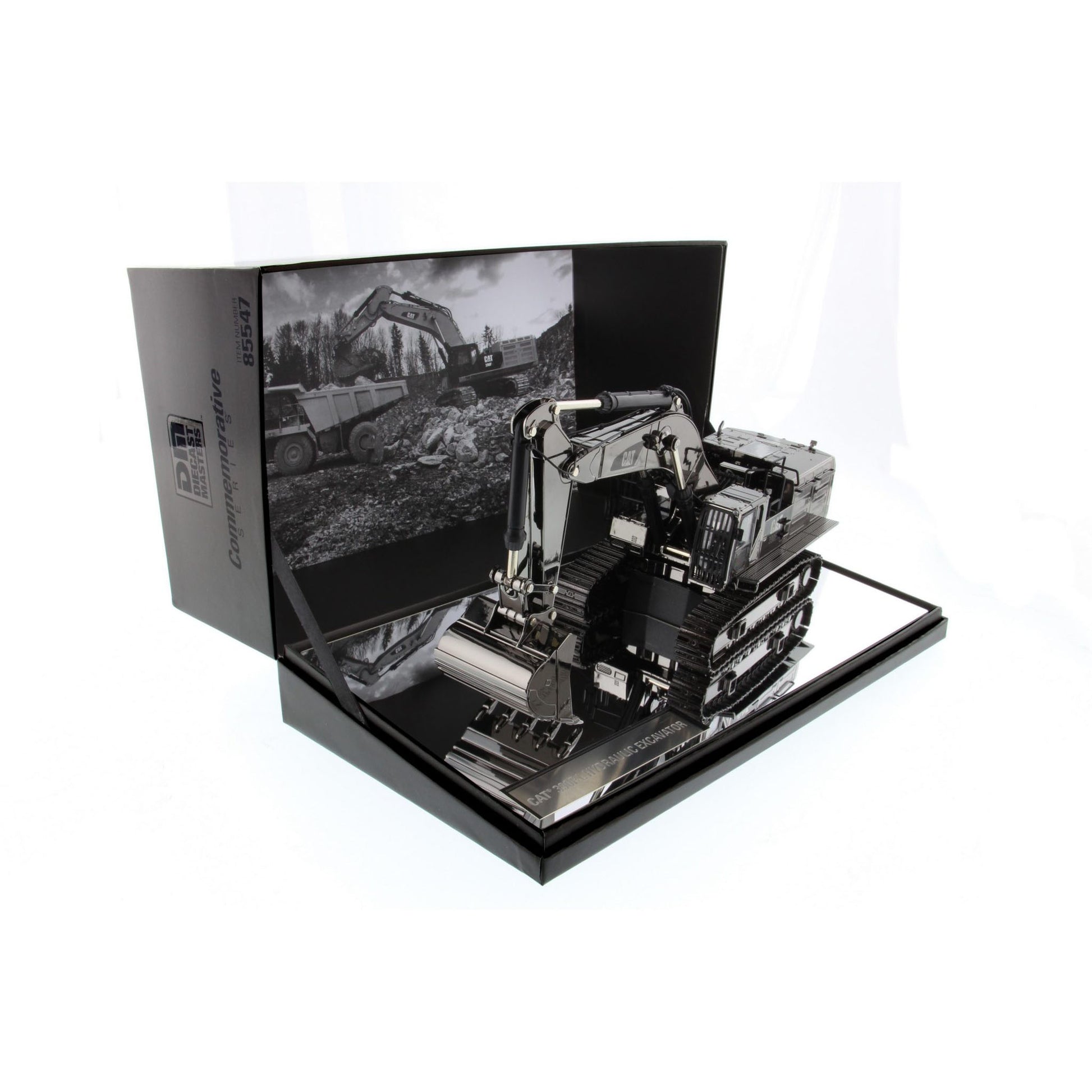 A  model of a black and silver excavator displayed inside its open black presentation box, which features a black-and-white construction scene printed on the inner flap.