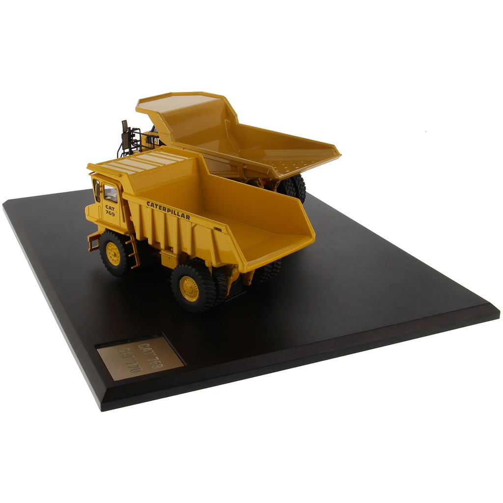 Models of Caterpillar 769 Off Highway Dump Truck (1963-1965) & Caterpillar 770 Off Highway Dump Truck (2013-Current) Mounted on a Black Base on a White Background