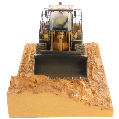 1:50th Scale Diecast Model of a Caterpillar 966M Wheel Loader with a Weathered Paint Scheme on a Tan Construction Site Base Plate on a White Background