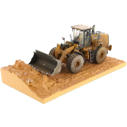 1:50th Scale Diecast Model of a Caterpillar 966M Wheel Loader with a Weathered Paint Scheme on a Tan Construction Site Base Plate on a White Background