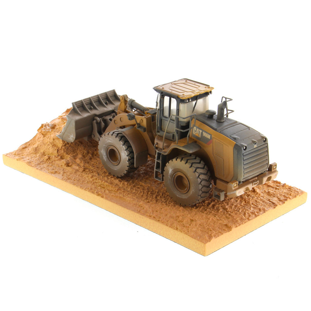1:50th Scale Diecast Model of a Caterpillar 966M Wheel Loader with a Weathered Paint Scheme on a Tan Construction Site Base Plate on a White Background