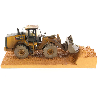 1:50th Scale Diecast Model of a Caterpillar 966M Wheel Loader with a Weathered Paint Scheme on a Tan Construction Site Base Plate on a White Background