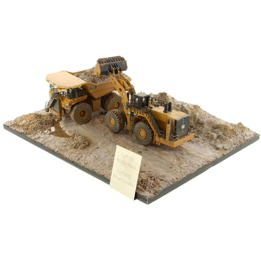 Model of a Caterpillar 994K Wheel Loader Loading a Model of a CAT 797 Mining Dump Truck Attached to a Base That is Made to Look Like a Rock & Dirt Construction Site on a White Background