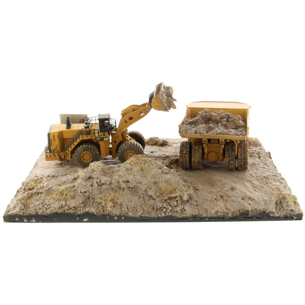 Model of a Caterpillar 994K Wheel Loader Loading a Model of a CAT 797 Mining Dump Truck Attached to a Base That is Made to Look Like a Rock & Dirt Construction Site on a White Background