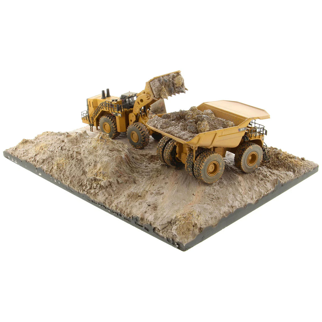 Model of a Caterpillar 994K Wheel Loader Loading a Model of a CAT 797 Mining Dump Truck Attached to a Base That is Made to Look Like a Rock & Dirt Construction Site on a White Background