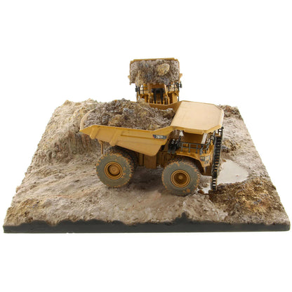 Model of a Caterpillar 994K Wheel Loader Loading a Model of a CAT 797 Mining Dump Truck Attached to a Base That is Made to Look Like a Rock & Dirt Construction Site on a White Background