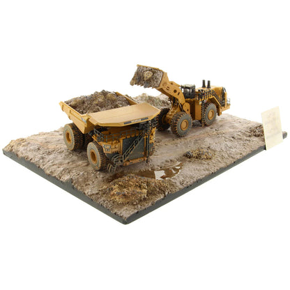 Model of a Caterpillar 994K Wheel Loader Loading a Model of a CAT 797 Mining Dump Truck Attached to a Base That is Made to Look Like a Rock & Dirt Construction Site on a White Background