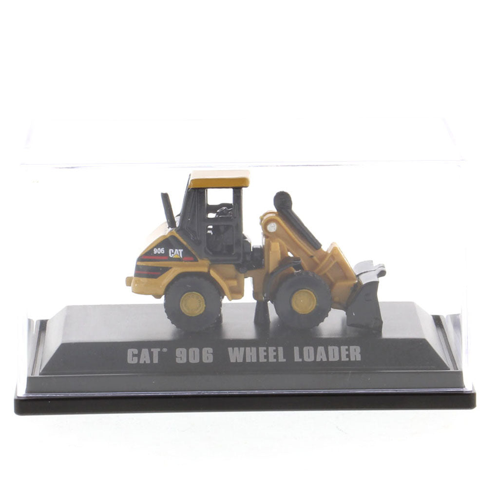 A miniature yellow and black CAT 906 wheel loader toy model displayed on a black base with 'CAT 906 WHEEL LOADER' printed on it, under a clear plastic cover.