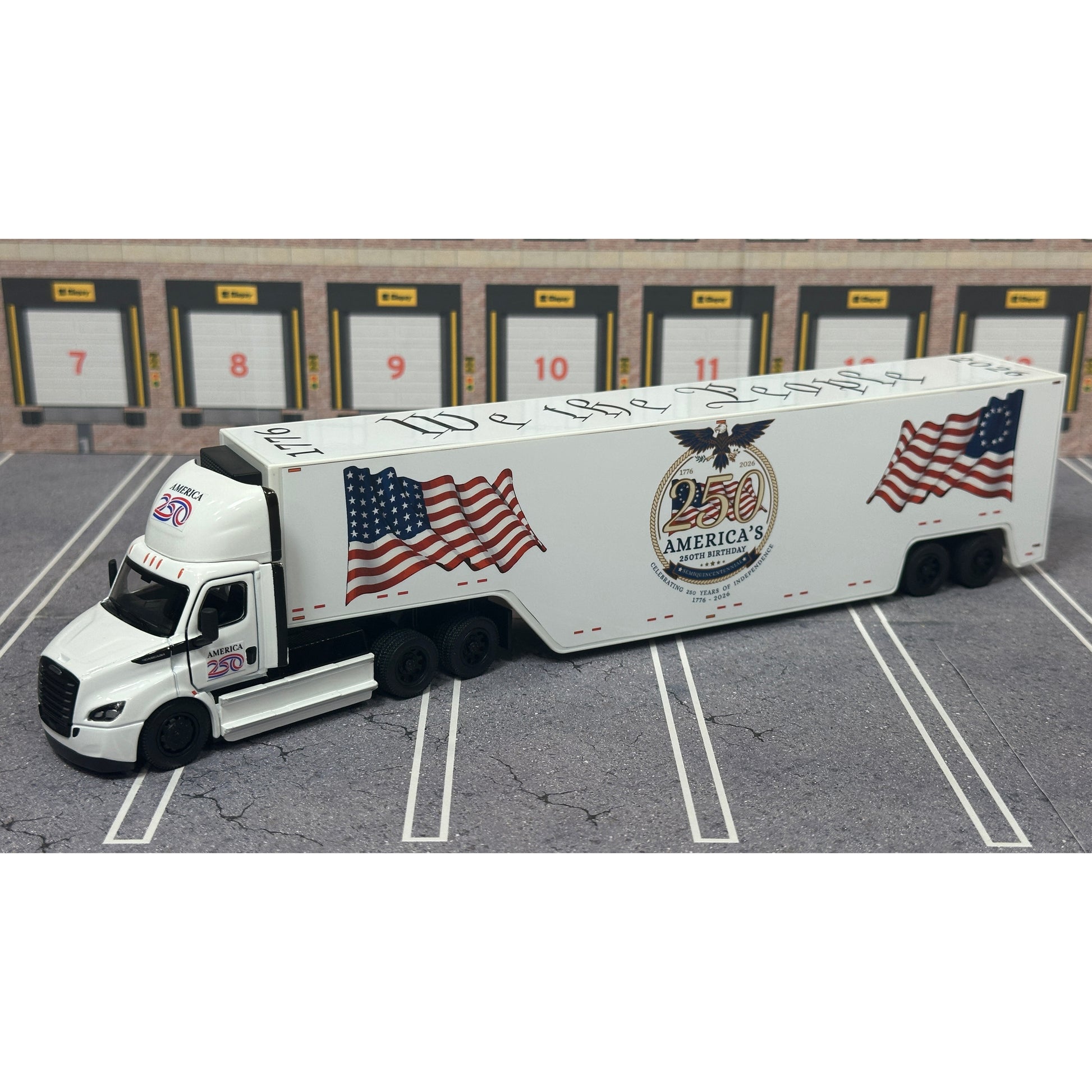 A diecast model of a Freightliner Cascadia semi-truck parked in a simulated parking lot. The trailer features a detailed historical design celebrating the United States' 250th anniversary with 'We the People' written on the side, alongside an American flag, eagle, and city skyline graphic with the text 'Land of the Free Home of the Brave' and 'United We Stand'.