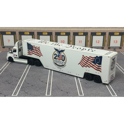 A diecast model of a white Freightliner Cascadia semi-truck with a long trailer decorated with American flags and a '250th Anniversary' logo, parked in a gray parking lot with a truck dock backdrop.