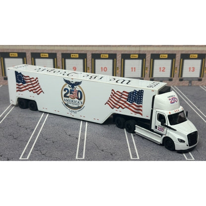 A diecast model of a white Freightliner Cascadia semi-truck with a long trailer decorated with American flags and a '250th Anniversary' logo, parked in a gray parking lot with a truck dock backdrop.