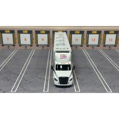 A diecast model of a white Freightliner Cascadia semi-truck with a long trailer decorated with American flags and a '250th Anniversary' logo, parked in a gray parking lot with a truck dock backdrop.