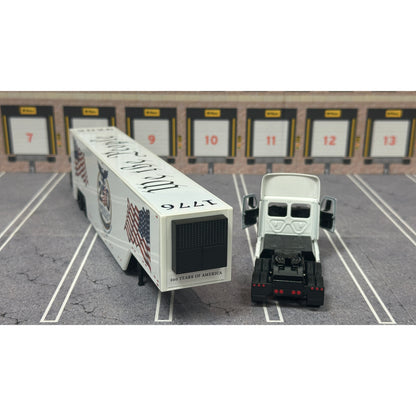 A diecast model of a white Freightliner Cascadia semi-truck with a long trailer decorated with American flags and a '250th Anniversary' logo, parked in a gray parking lot with a truck dock backdrop.
