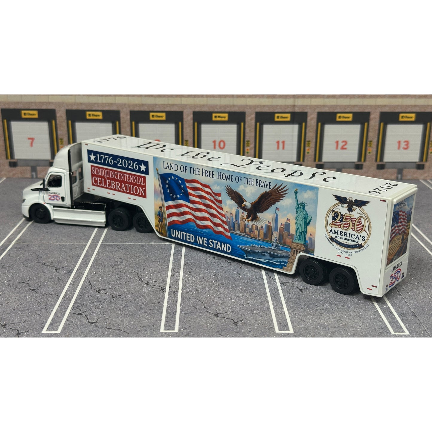 A diecast model of a Freightliner Cascadia semi-truck parked in a simulated parking lot. The trailer features a detailed historical design celebrating the United States' 250th anniversary with 'We the People' written on the top, alongside an American flag, eagle, and city skyline graphic with the text 'Land of the Free Home of the Brave' and 'United We Stand'.