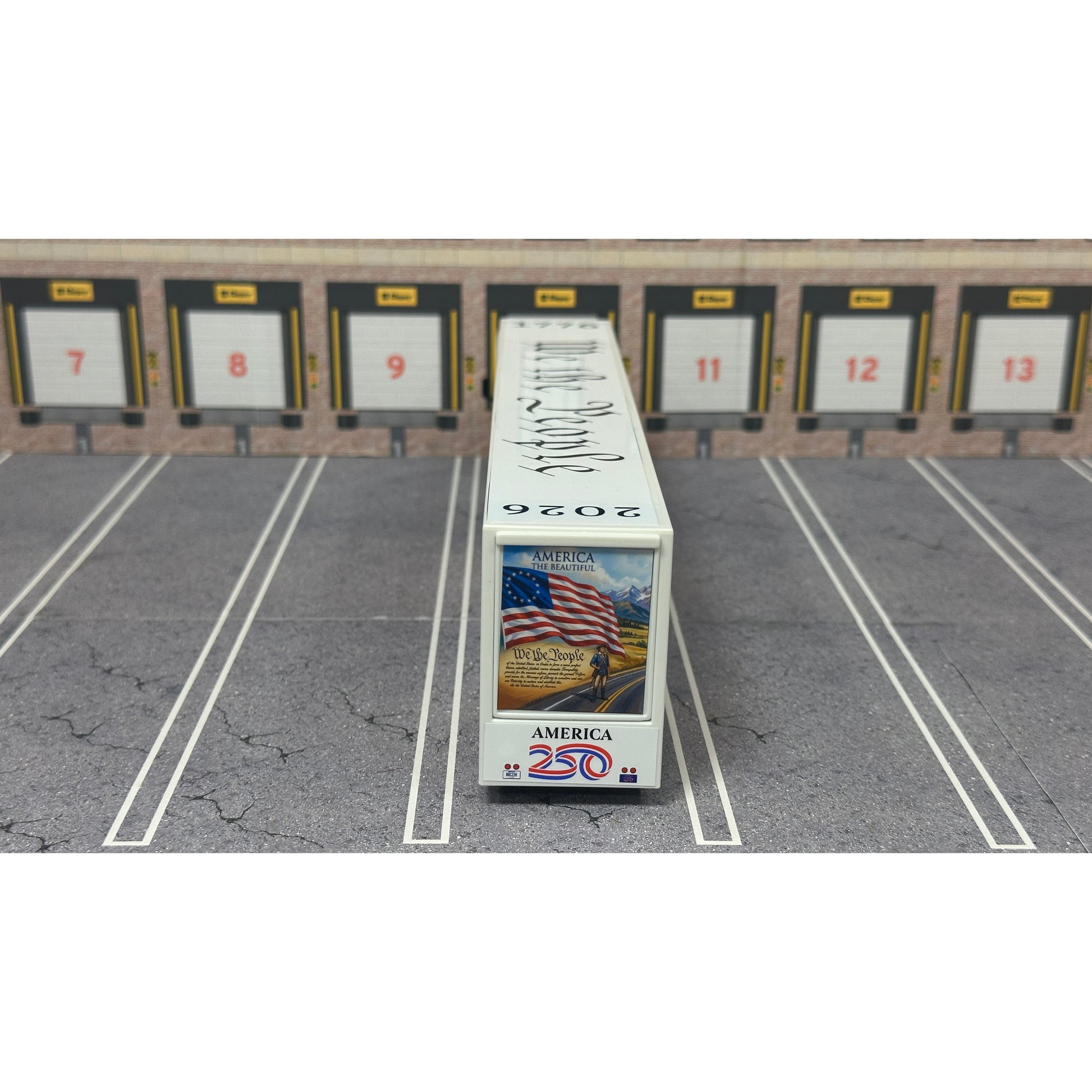 A diecast model of a Freightliner Cascadia semi-truck parked in a simulated parking lot. The trailer features a detailed historical design celebrating the United States' 250th anniversary with 'We the People' written on the top, alongside an American flag, eagle, and city skyline graphic with the text 'Land of the Free Home of the Brave' and 'United We Stand'.