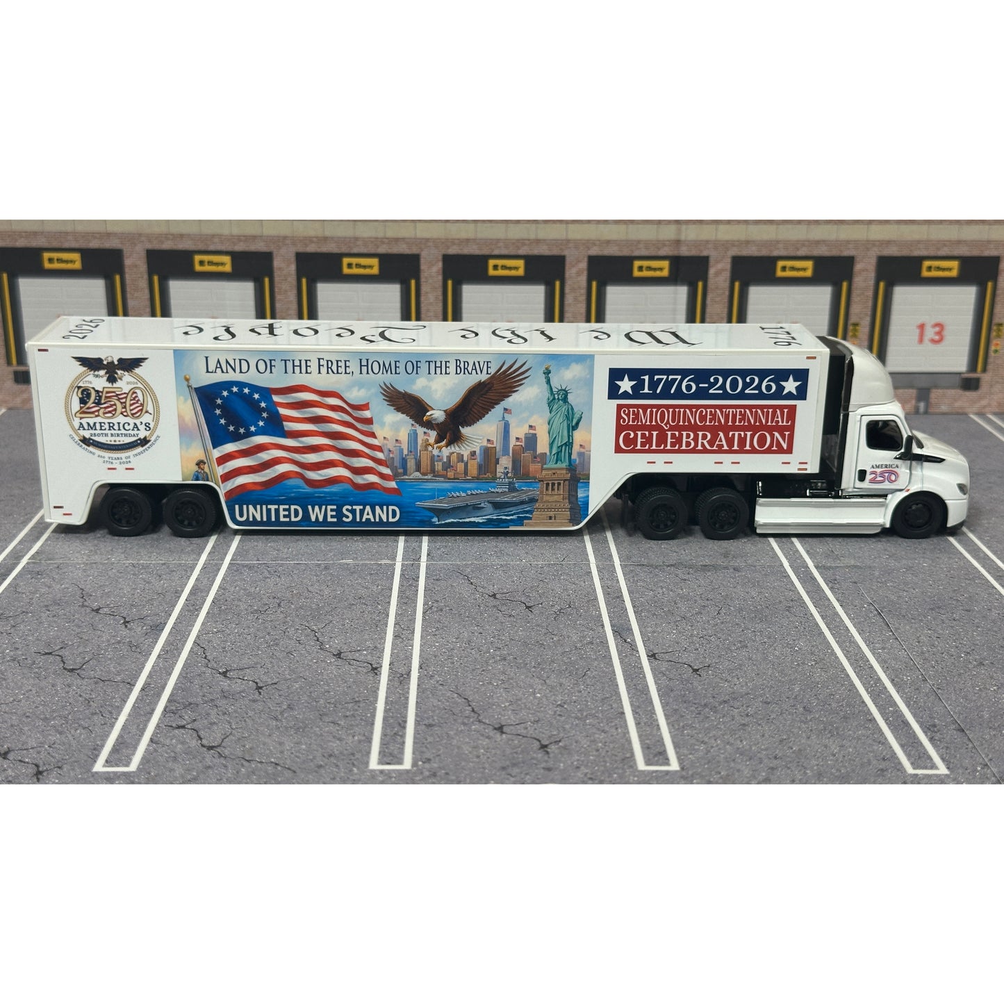 A diecast model of a Freightliner Cascadia semi-truck parked in a simulated parking lot. The trailer features a detailed historical design celebrating the United States' 250th anniversary with 'We the People' written on the top, alongside an American flag, eagle, and city skyline graphic with the text 'Land of the Free Home of the Brave' and 'United We Stand'.