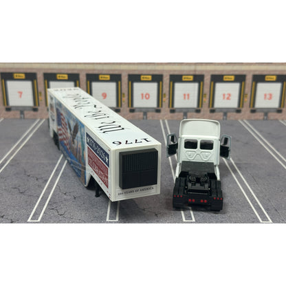 A diecast model of a Freightliner Cascadia semi-truck parked in a simulated parking lot. The trailer features a detailed historical design celebrating the United States' 250th anniversary with 'We the People' written on the top, alongside an American flag, eagle, and city skyline graphic with the text 'Land of the Free Home of the Brave' and 'United We Stand'.