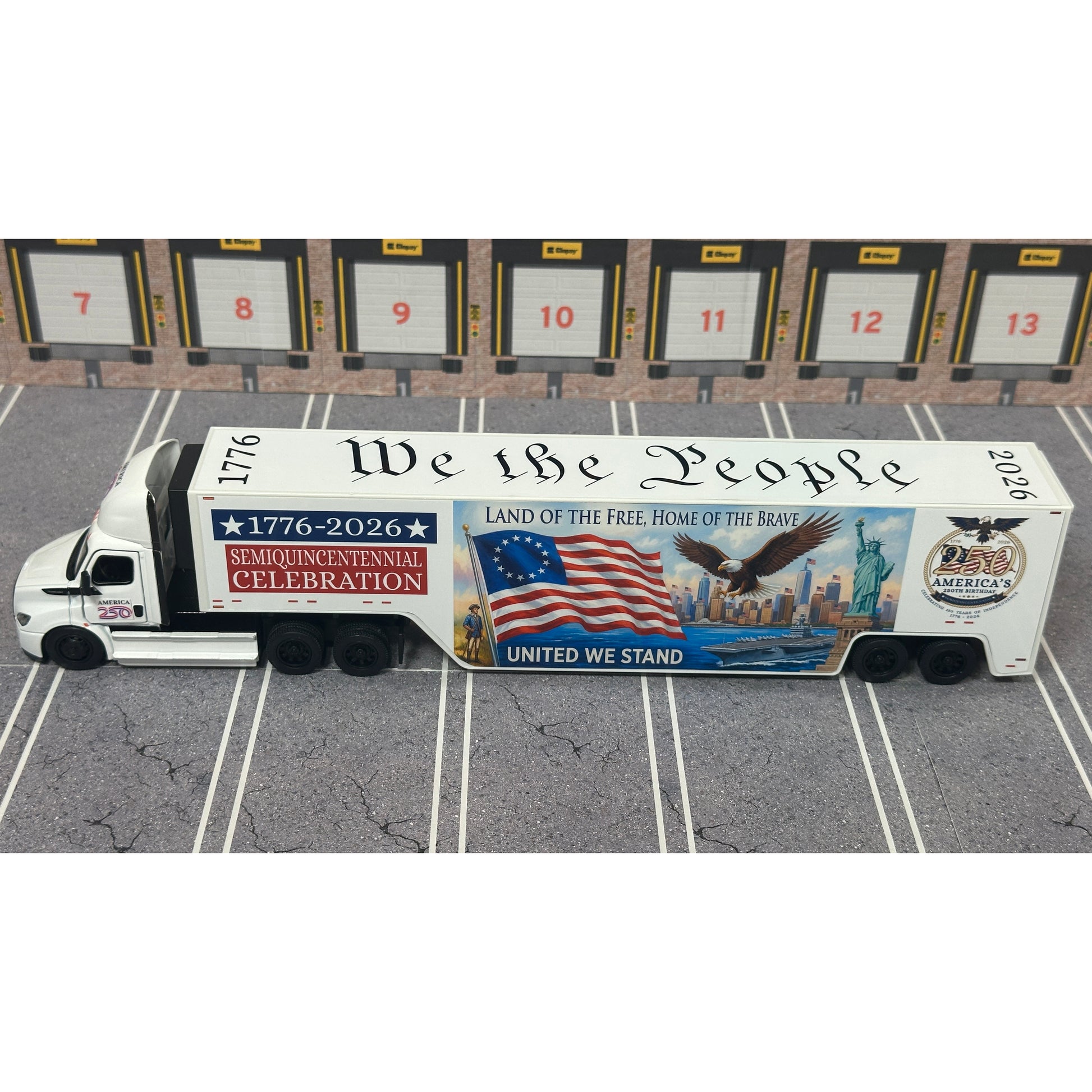 A diecast model of a Freightliner Cascadia semi-truck parked in a simulated parking lot. The trailer features a detailed historical design celebrating the United States' 250th anniversary with 'We the People' written on the top, alongside an American flag, eagle, and city skyline graphic with the text 'Land of the Free Home of the Brave' and 'United We Stand'.