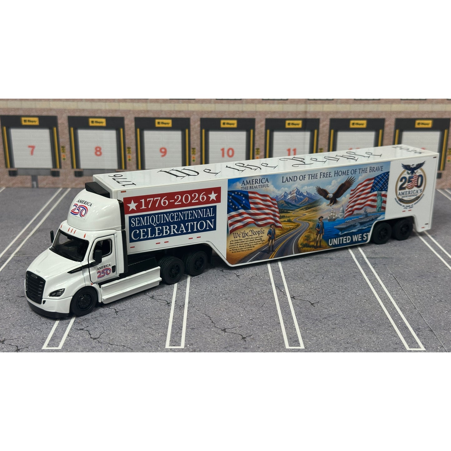 A diecast model of a Freightliner Cascadia semi-truck parked in a simulated parking lot. The trailer features a detailed historical design celebrating the United States' 250th anniversary with 'We the People' written on the top, alongside an American flag, eagle, and city skyline graphic with the text 'Land of the Free Home of the Brave' and 'United We Stand'.
