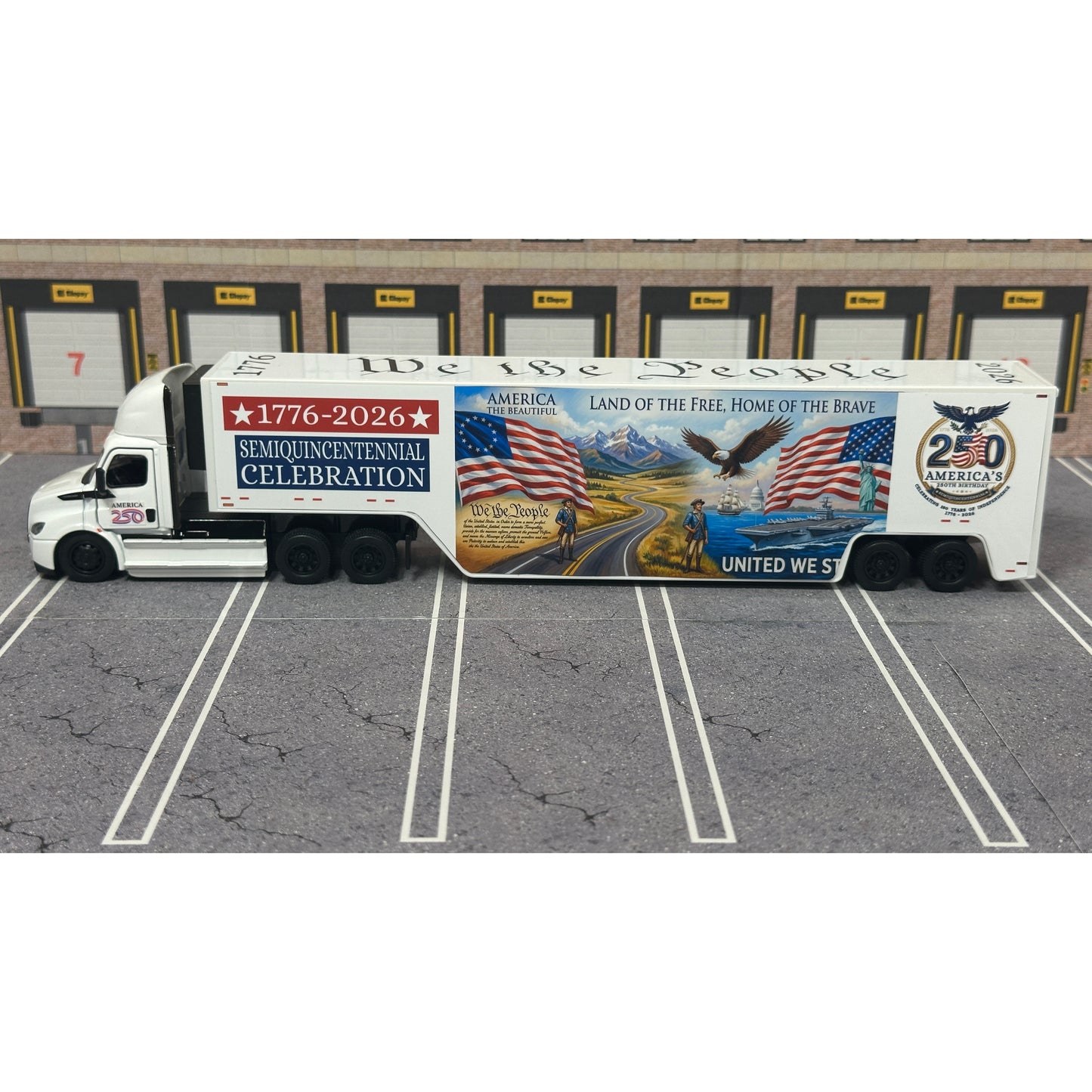 A diecast model of a Freightliner Cascadia semi-truck parked in a simulated parking lot. The trailer features a detailed historical design celebrating the United States' 250th anniversary with 'We the People' written on the top, alongside an American flag, eagle, and city skyline graphic with the text 'Land of the Free Home of the Brave' and 'United We Stand'.