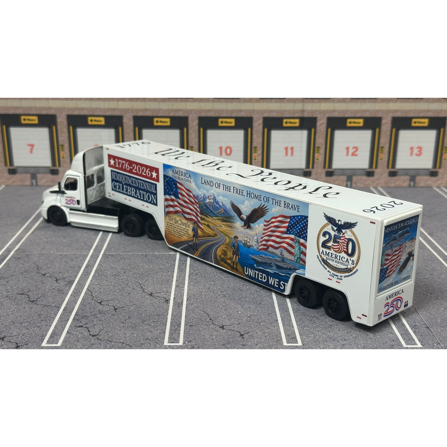 A diecast model of a Freightliner Cascadia semi-truck parked in a simulated parking lot. The trailer features a detailed historical design celebrating the United States' 250th anniversary with 'We the People' written on the top, alongside an American flag, eagle, and city skyline graphic with the text 'Land of the Free Home of the Brave' and 'United We Stand'.