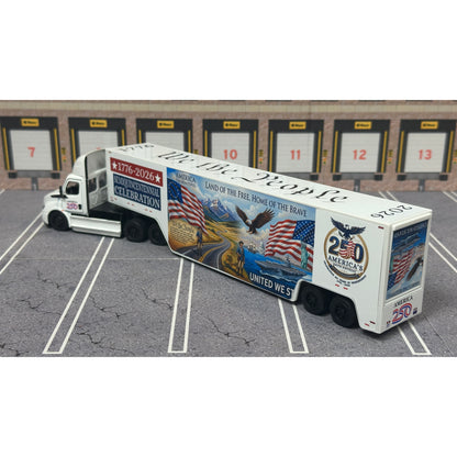 A diecast model of a Freightliner Cascadia semi-truck parked in a simulated parking lot. The trailer features a detailed historical design celebrating the United States' 250th anniversary with 'We the People' written on the top, alongside an American flag, eagle, and city skyline graphic with the text 'Land of the Free Home of the Brave' and 'United We Stand'.
